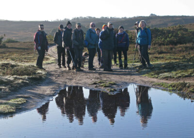 Photo of walkers' reflections in a large puddle – December 13, 2025